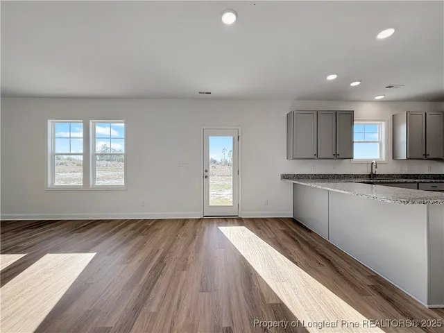 a view of empty room with wooden floor and kitchen