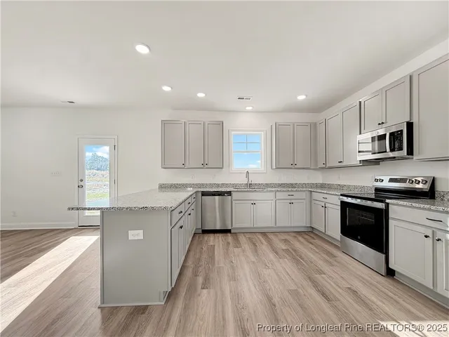 a large kitchen with granite countertop a large counter top space a sink stainless steel appliances and cabinets