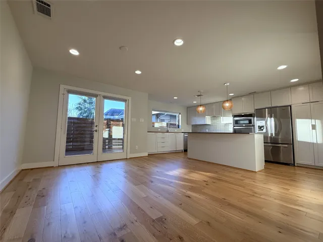 a view of an empty room with wooden floor and a kitchen