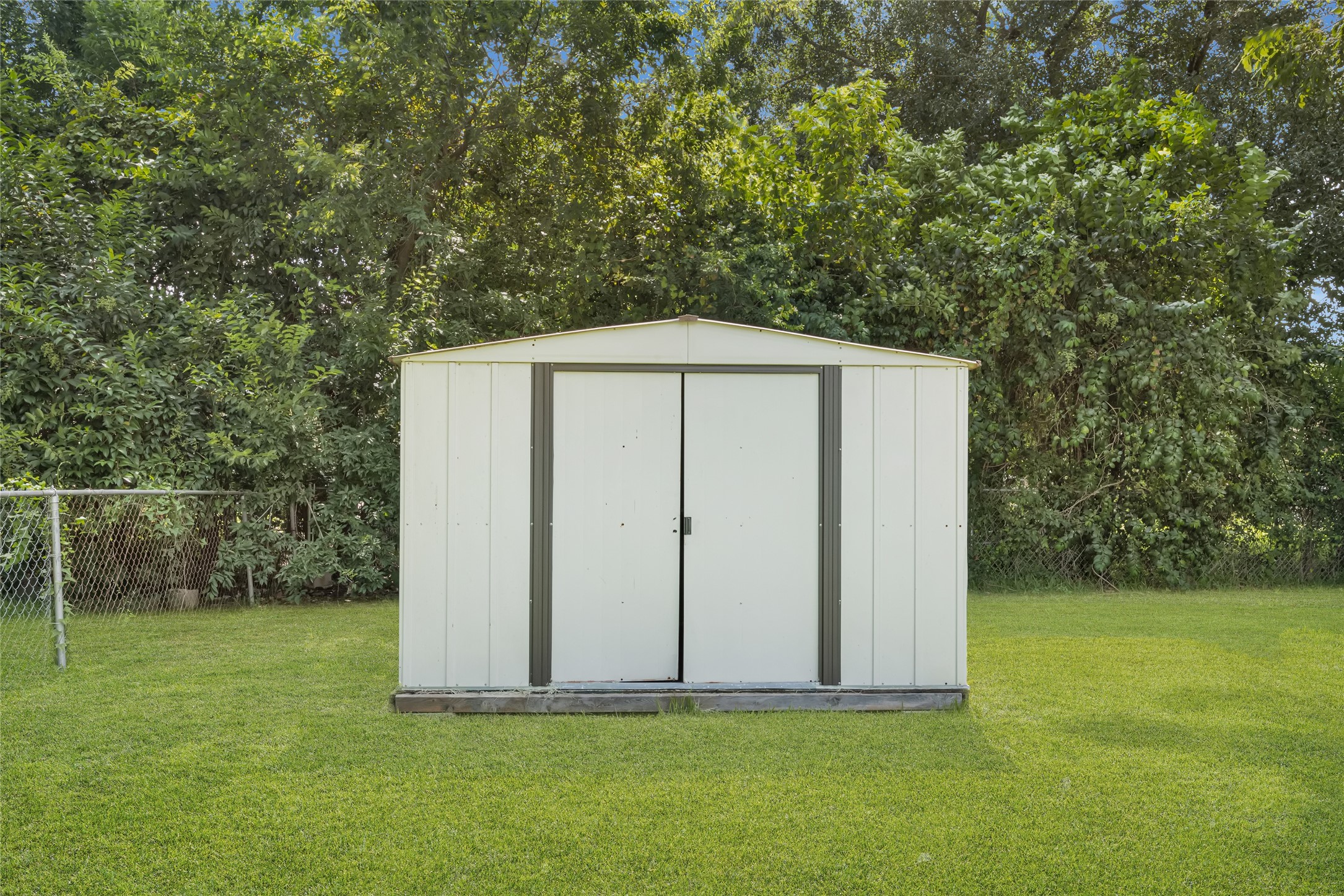9210 Compton Street Houston, TX 77016 - Photo 46 of 50 Spacious metal storage shed in a lush, green backyard, ideal for organizing tools and equipment.