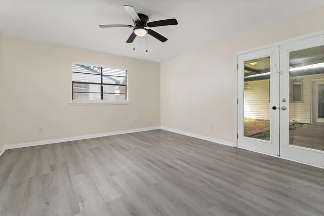 an empty room with wooden floor chandelier fan and windows