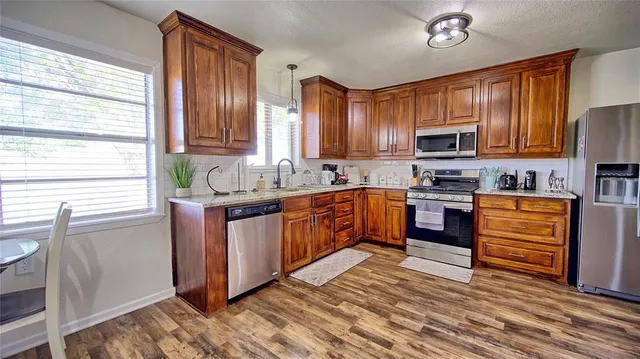 a kitchen with stainless steel appliances kitchen island granite countertop a stove top oven a sink dishwasher a dining table and chairs with wooden floor