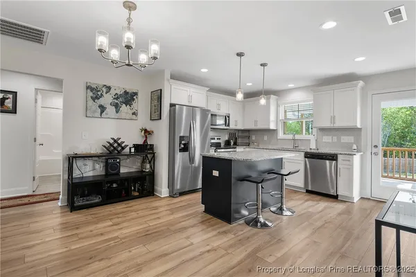 a kitchen with stainless steel appliances kitchen island granite countertop a refrigerator a stove a sink dishwasher and a dining table with wooden floor