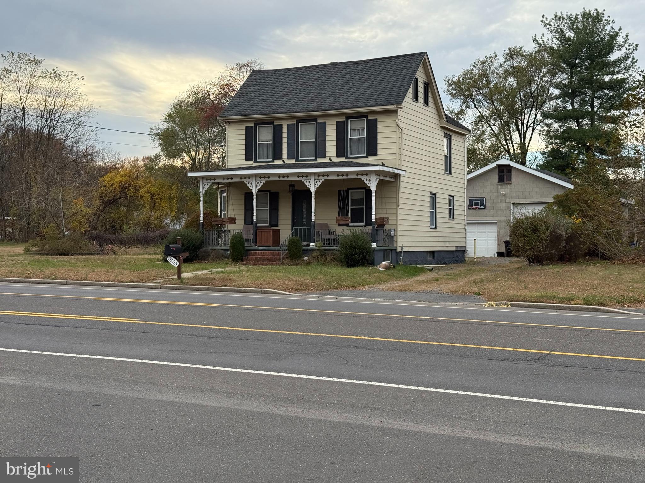a view of a white house with a small yard and large trees