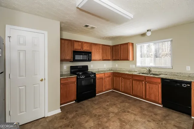 a kitchen with stainless steel appliances granite countertop a stove top oven a sink dishwasher a refrigerator and a microwave oven with wooden cabinets