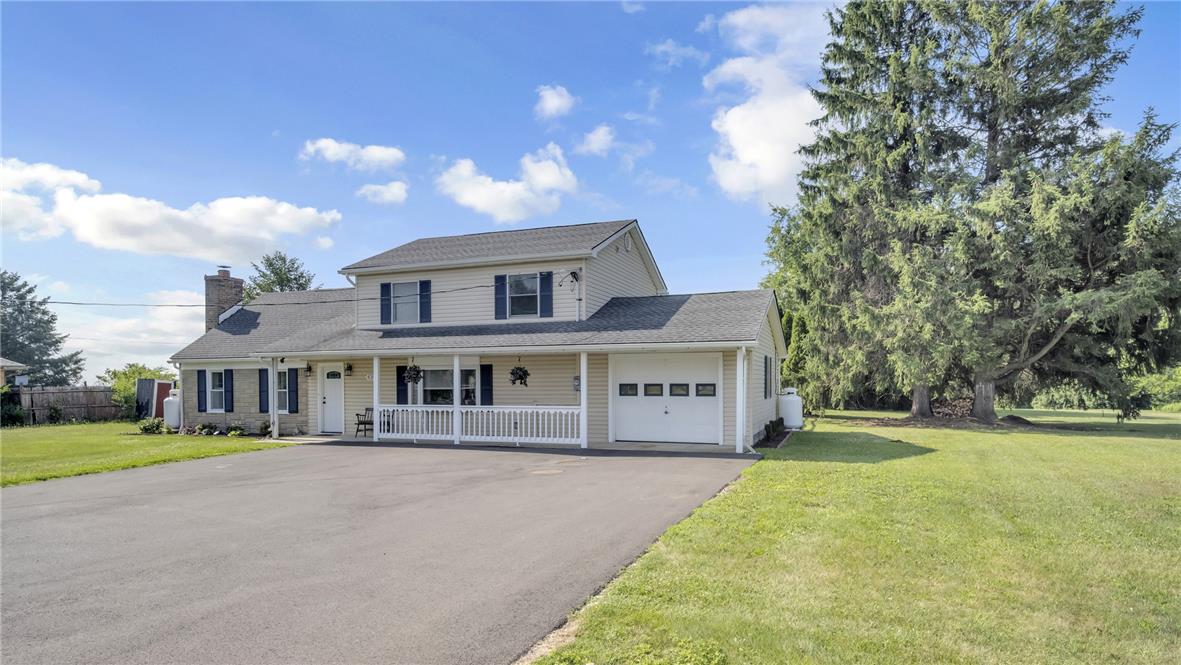 A classic facade with a welcoming porch and attached garage, nestled beside mature trees.