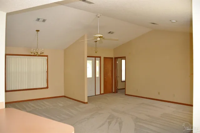 an empty room with chandelier fan and windows