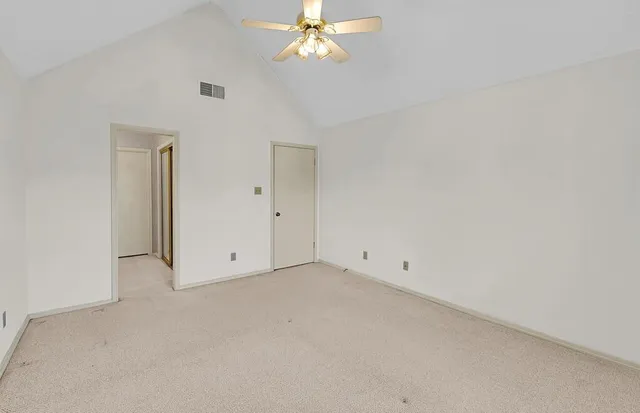 an empty room with a chandelier fan and windows