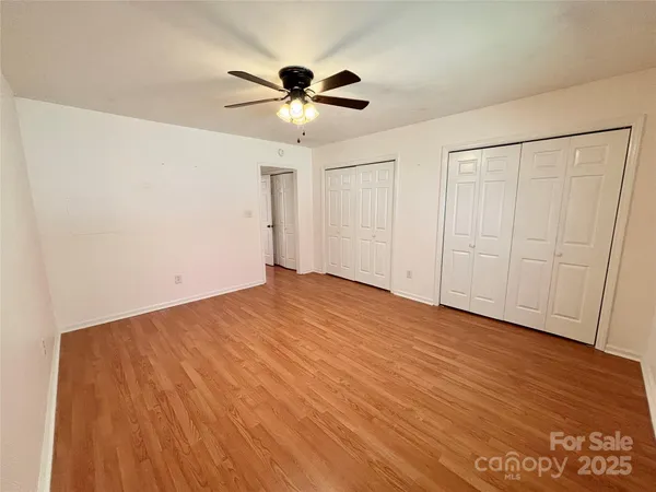 an empty room with wooden floor fan and windows
