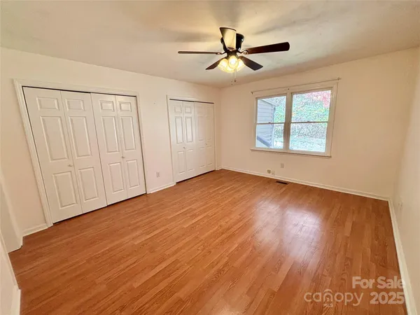 an empty room with wooden floor fan and windows