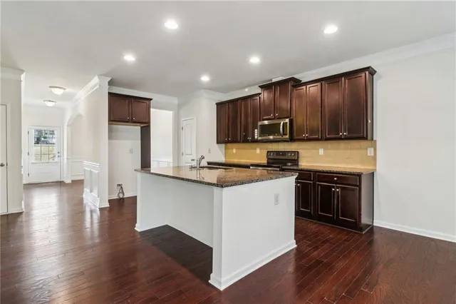 a kitchen with stainless steel appliances granite countertop wooden cabinets a stove a sink and a wooden floor