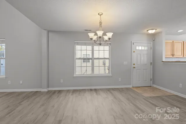 an empty room with wooden floor chandelier and windows