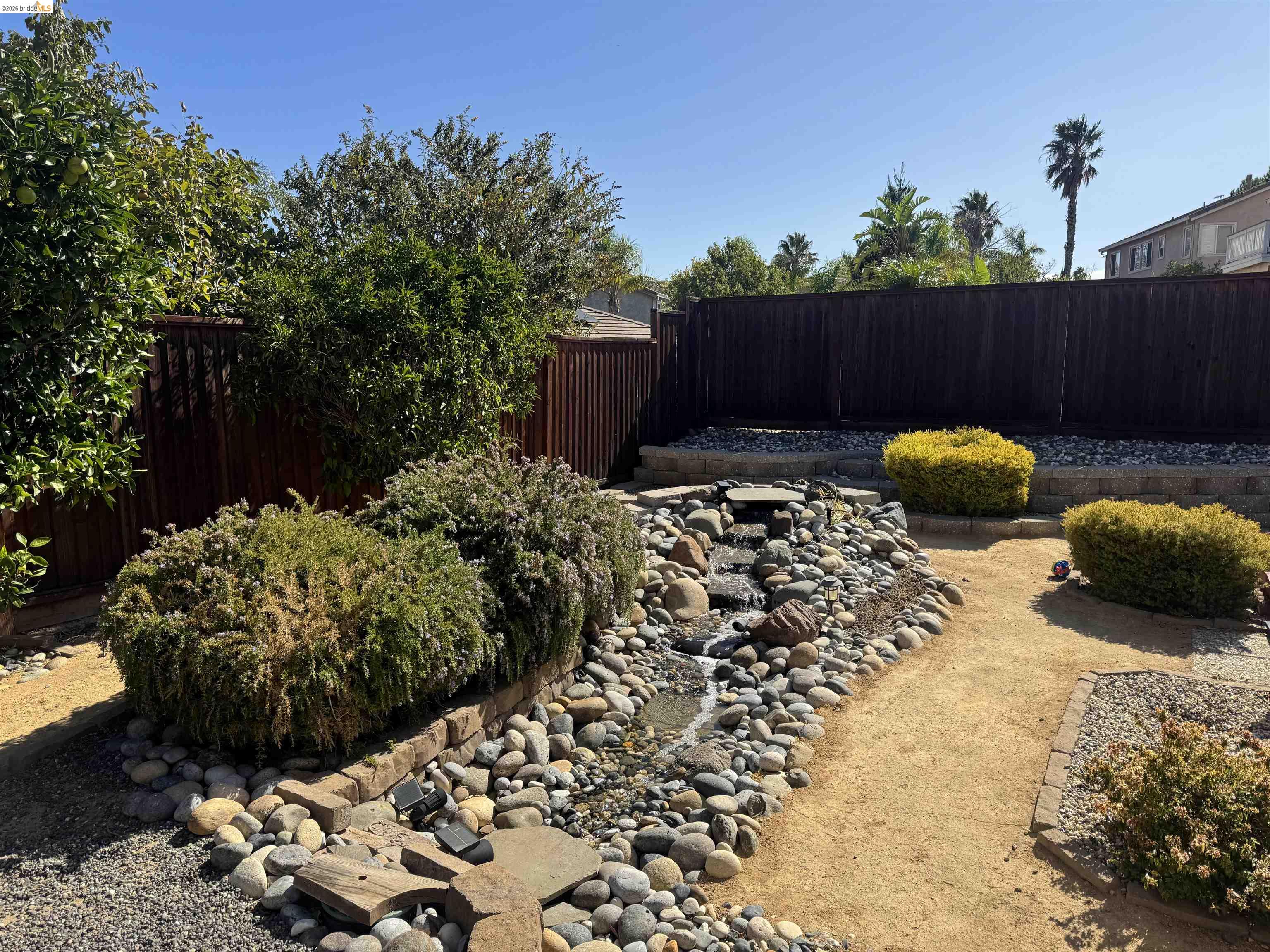2385 Fieldgate Drive Pittsburg, CA 94565 - Photo 5 of 8 Landscaped backyard featuring a tiered rock water feature, mature shrubs, and a privacy fence