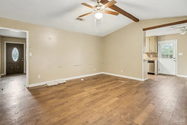 an empty room with chandelier fan and windows