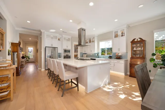 a open kitchen with stainless steel appliances kitchen island granite countertop a refrigerator a sink a stove and white cabinets with wooden floor