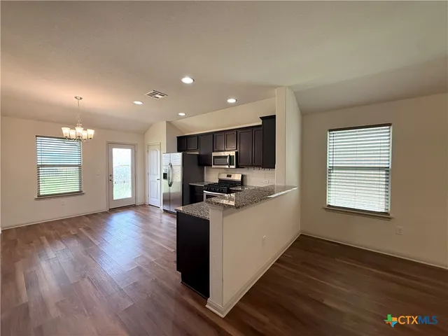 a kitchen with stainless steel appliances granite countertop a stove top oven a sink dishwasher and a refrigerator with wooden floor