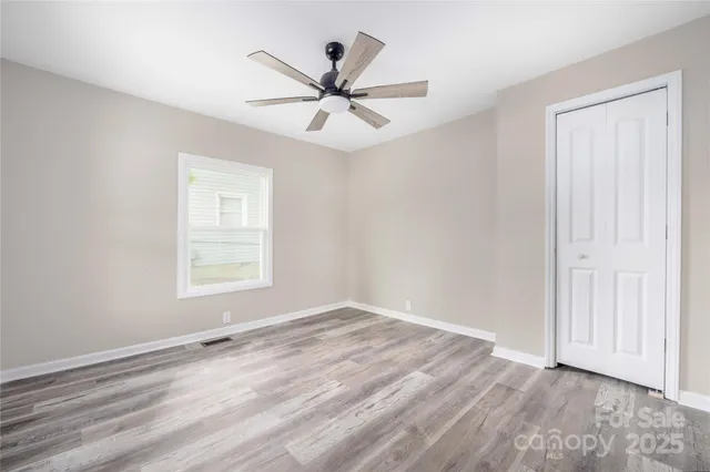an empty room with wooden floor fan and windows