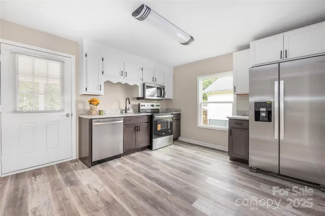 a kitchen with granite countertop a refrigerator a sink a stove and white cabinets