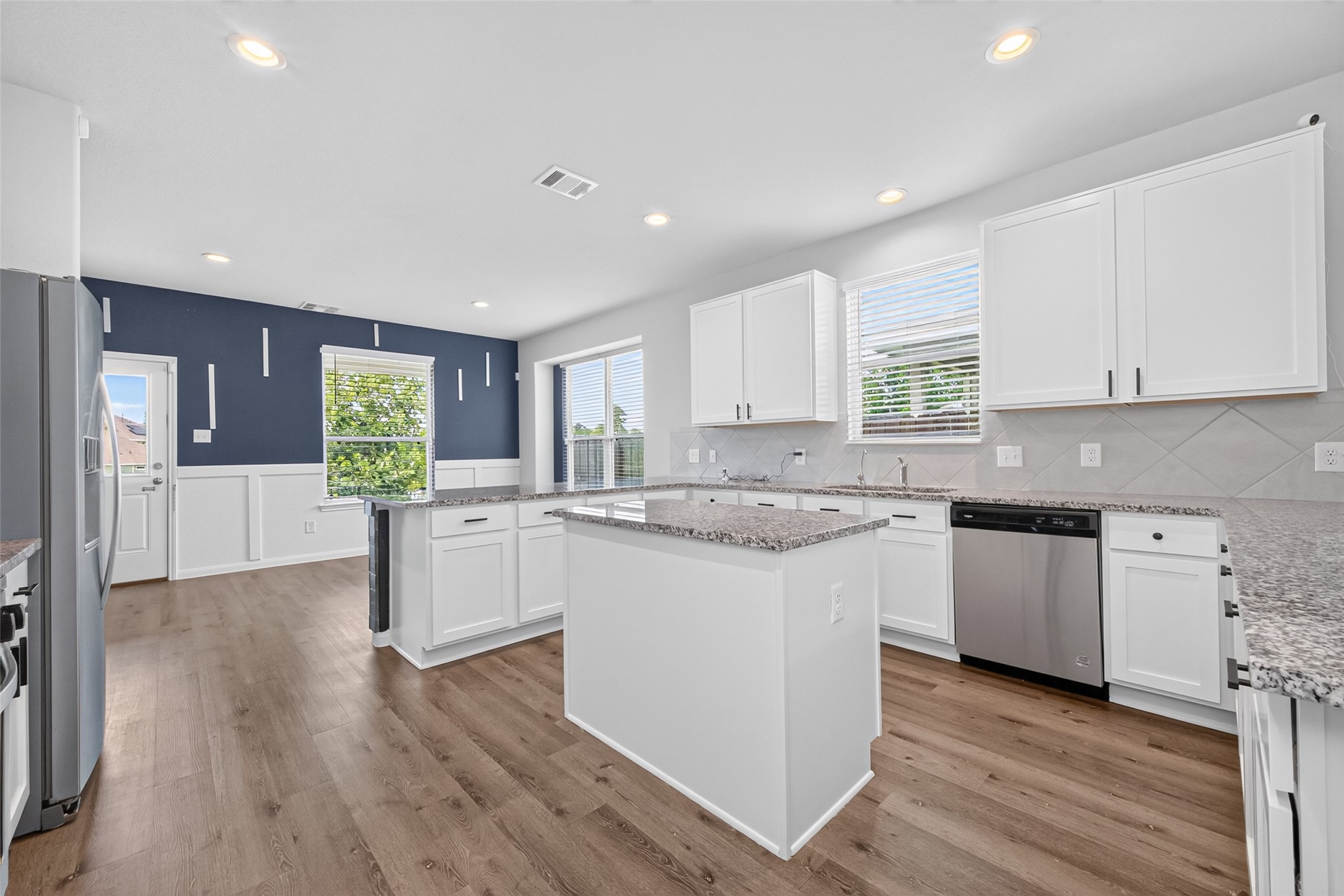 2526 Sturgeon Way Conroe, TX 77384 - Photo 5 of 49 This modern kitchen features sleek white cabinetry, granite countertops, and stainless steel appliances. It has an island for additional prep space and large windows that allow natural light to fill the room, highlighting the elegant wood flooring.