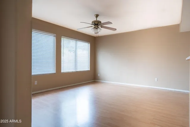 an empty room with wooden floor chandelier fan and windows