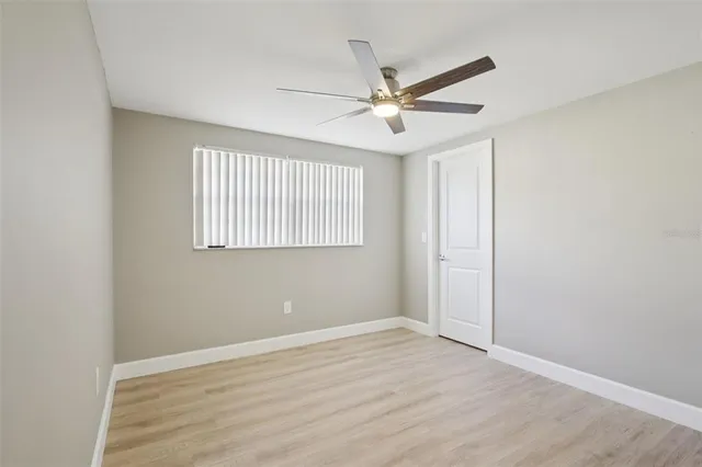 an empty room with wooden floor fan and windows