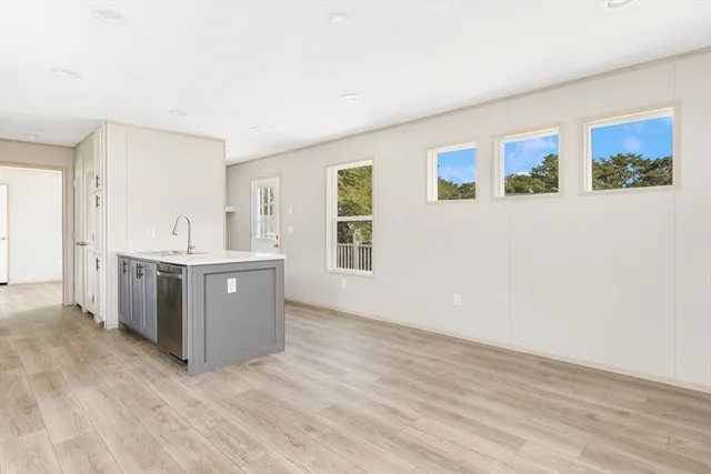 a living room with stainless steel appliances kitchen island wooden floors and white walls