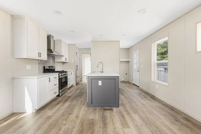 a large white kitchen with granite countertop a stove top oven a sink dishwasher and a refrigerator with wooden floor