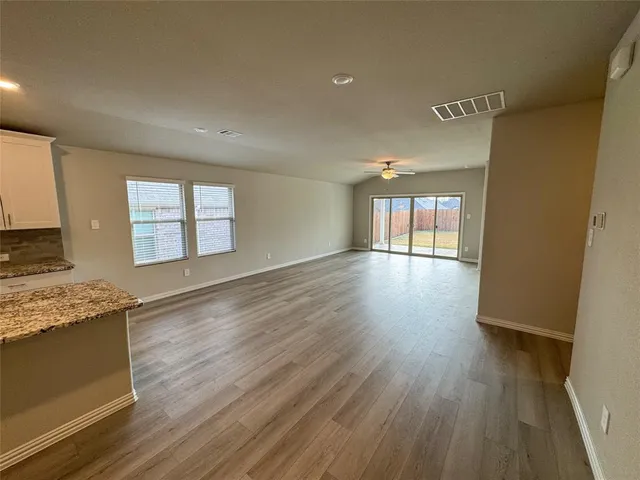 a view of a kitchen and an empty room with wooden floor and a window
