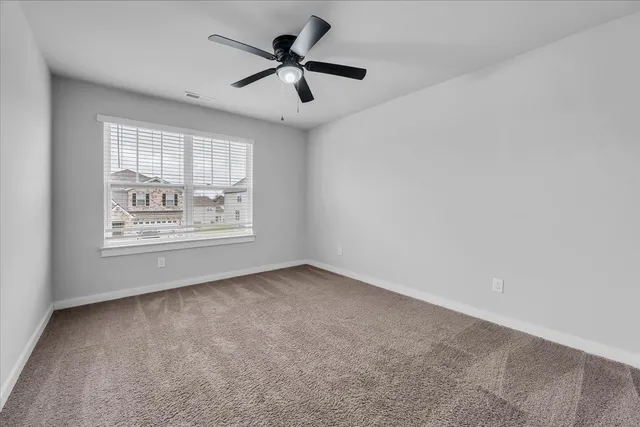an empty room with a chandelier fan and windows