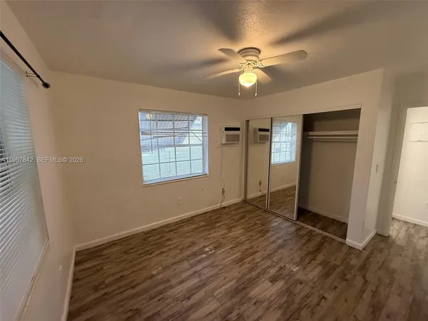 an empty room with wooden floor fan and windows