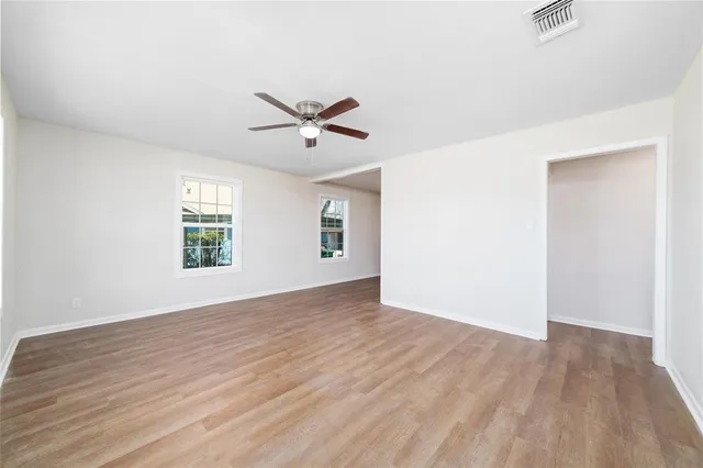 an empty room with wooden floor chandelier fan and windows