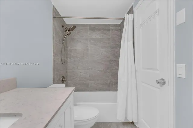 a bathroom with a granite countertop bathtub shower sink vanity and toilet
