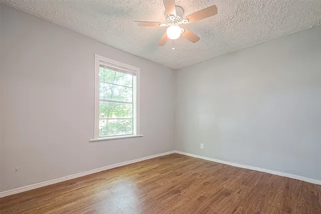 an empty room with wooden floor fan and windows