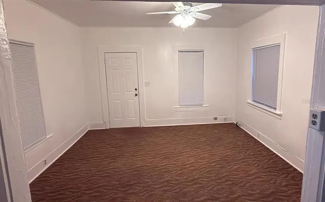 a view of an empty room with wooden floor and fan