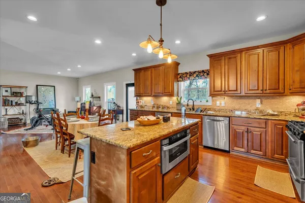 a open kitchen with stainless steel appliances granite countertop a stove top oven a sink dishwasher and white cabinets with wooden floor