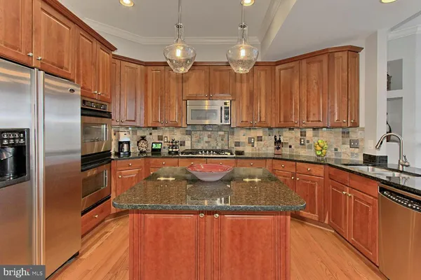 a kitchen with granite countertop stainless steel appliances a sink dishwasher a refrigerator a stove top oven and wooden floor