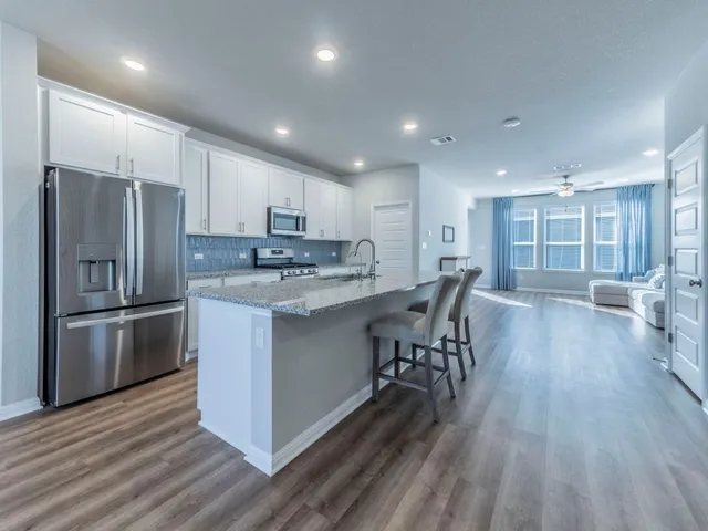 a kitchen with stainless steel appliances granite countertop a refrigerator a stove top oven a sink dishwasher a dining table and chairs with wooden floor