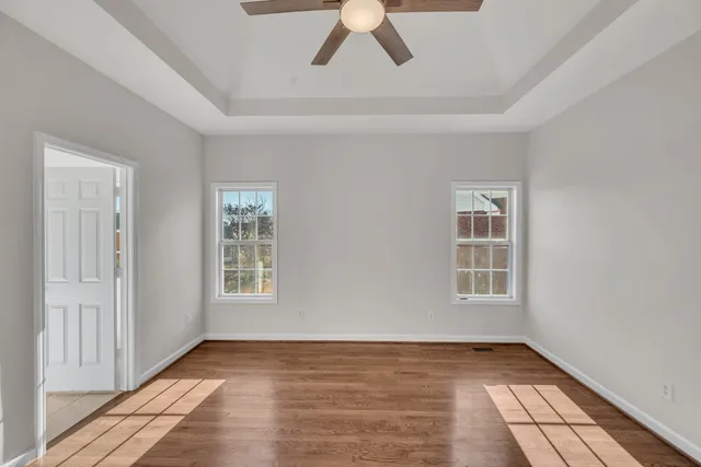 an empty room with wooden floor chandelier fan and windows