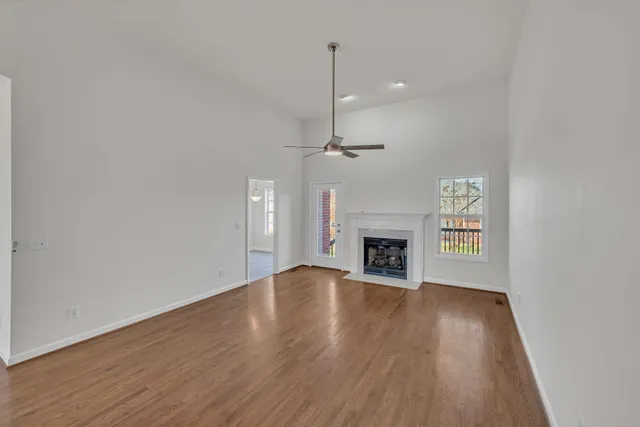 a view of an empty room with wooden floor fireplace and a window