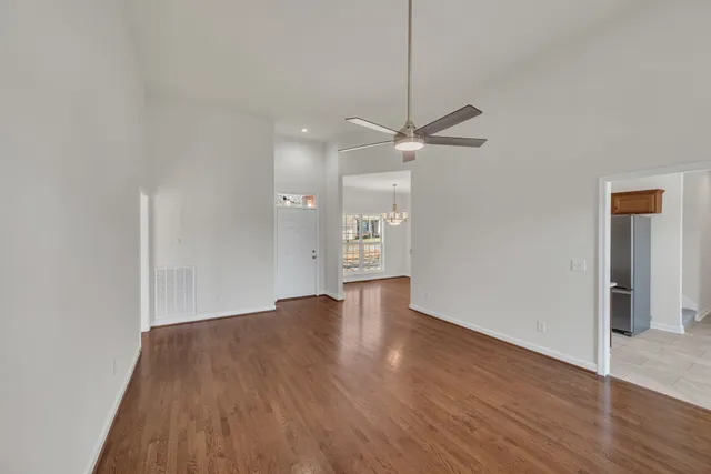 a view of an empty room with wooden floor and a ceiling fan