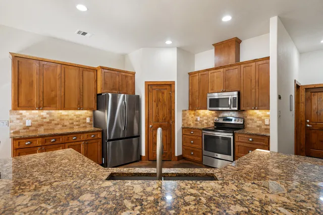 a kitchen with stainless steel appliances granite countertop a refrigerator a sink dishwasher a stove and a sink with wooden floor