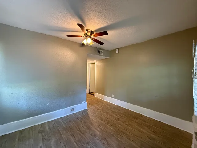 an empty room with wooden floor fan and windows