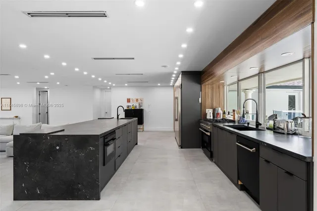 a large kitchen with a large counter top a sink stainless steel appliances and cabinets