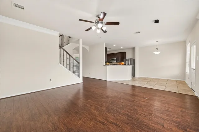 a view of an empty room with wooden floor and a ceiling fan