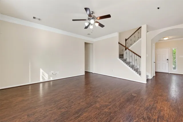 a view of an empty room with wooden floor and a ceiling fan