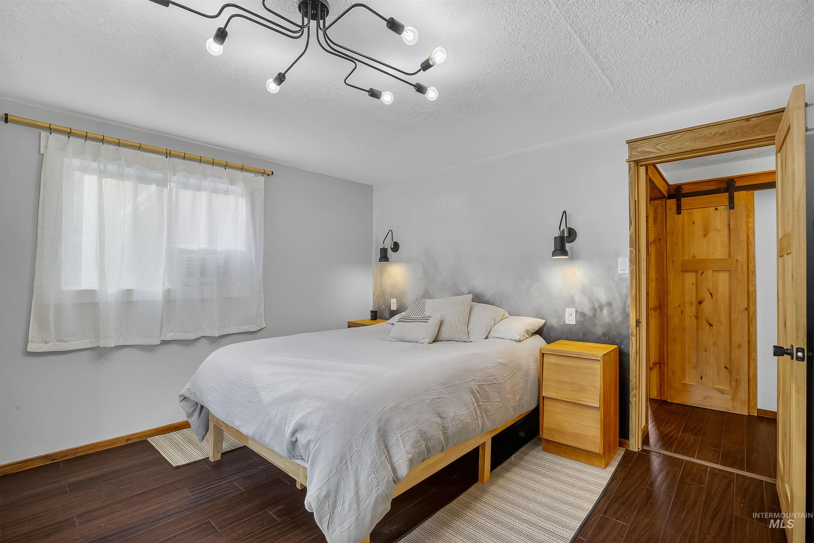 2157 Lukes Gulch Road Stites, ID 83552 - Photo 31 of 50 Bedroom with dark wood-type flooring, a barn door, a textured ceiling, and a chandelier