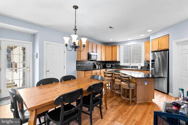 a kitchen with stainless steel appliances granite countertop a stove a refrigerator a kitchen island a sink dishwasher a dining table and chairs with wooden floor