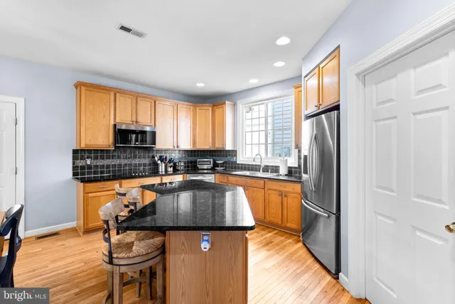 a kitchen with stainless steel appliances granite countertop a refrigerator a sink dishwasher a stove and white countertops with wooden floor