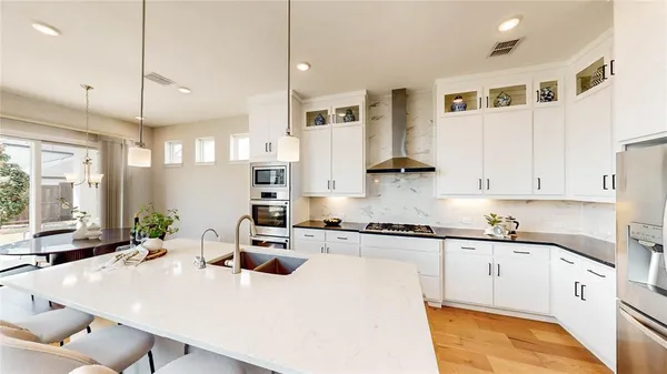 a kitchen with stainless steel appliances kitchen island granite countertop a stove a sink a refrigerator and white cabinets with wooden floor