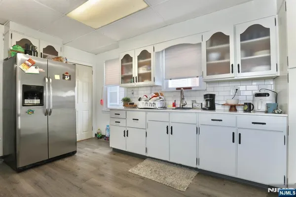 a kitchen with stainless steel appliances granite countertop a refrigerator a sink and white cabinets with wooden floor